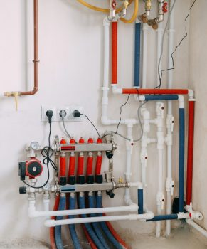 Detailed view of an intricate heating system setup featuring red and blue color-coded pipes, valves, and gauges. Connection diagram of a gas boiler with a underfloor heating system.